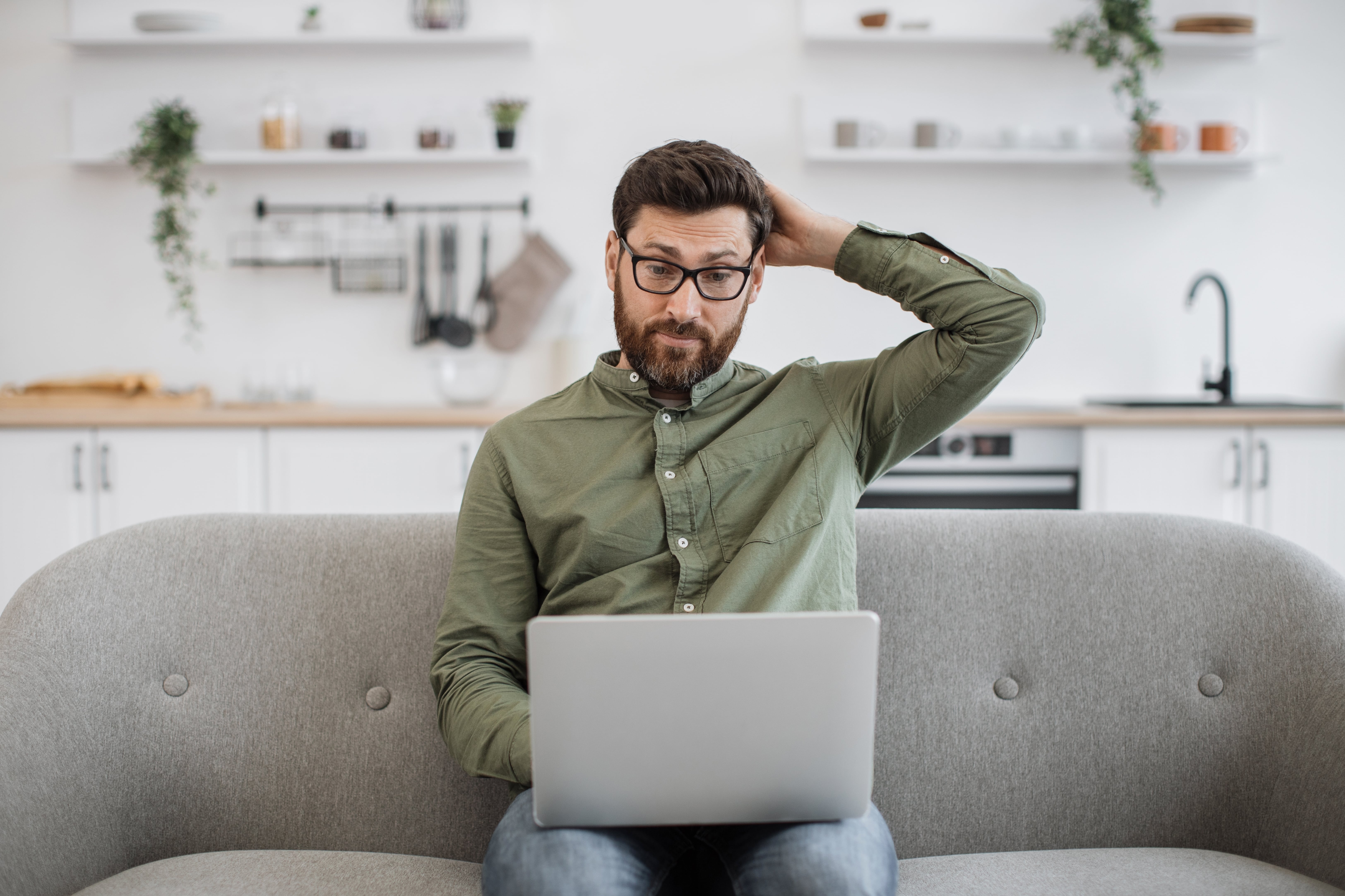 Confused man in glasses holding envelopes and looking at overflowing mailbox
